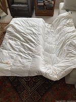 White down duvet spread out on a patterned rug and white couch, showing its size and some stains