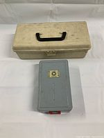 Top view photo of two plastic storage cases, one beige with black handle and one smaller gray case with clasp.