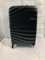 Front view of the black hard shell luggage showing wavy stripe pattern and American Tourister logo.