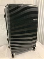 Front view of black hard shell suitcase with striped pattern and American Tourister branding.