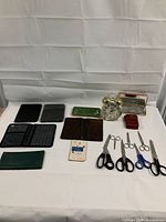 All items displayed together, showing passport wallet, checkbook folder, alarm clock, cigarette case, red box, and various scissors
