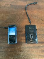 Nokia 5310 XpressMusic phone and Canon PowerShot SX310HS camera side by side on wooden surface.