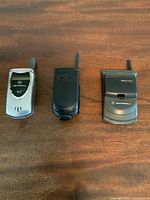 Photo showing the three older Motorola flip phones laid out on a wooden surface, highlighting their size and external antenna features.