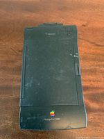 Front view of the Apple Newton MessagePad 2000 with visible retro Apple logo and visible wear and scratches on black casing.