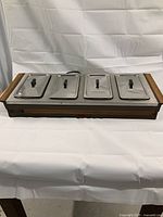 Full top and front view of the vintage buffet server showing four stainless steel trays with lids and the woodgrain trimmed base.