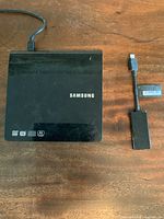 Top view of Samsung external DVD/CD player with USB adapter cable connected, showing the device on a wooden surface.
