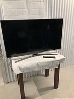Samsung 48 inch TV on a small table covered by white cloth, showing full unit and remote placed on the table.