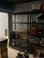 Heavy duty black plastic shelving unit with four empty shelves, positioned in a metal storage space.