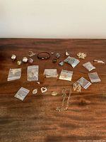 Assortment of rings, earrings, chains, pendants all laid out on a wooden surface, some pieces in plastic bags.