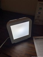 Front lit view of the Verilux HappyLight Compact energy lamp turned on, showing the light panel emitting white light.