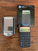 Top view of Compaq iPAQ Pocket PC and HP 10bII+ Financial Calculator with calculator turned on displaying zeros. Manual visible beside calculator.