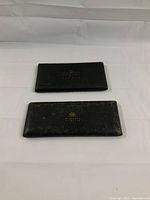 Two closed black drafting instrument cases placed on a white surface, showing wear and tear.