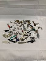 Full view of assorted vintage keychains and locks spread out on a white surface, showing a wide variety of items including padlocks, branded keychains, and novelty items.