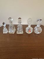 Front view of all five perfume bottles arranged in a row on wooden surface against a white background, showing variation in shape and stopper design.