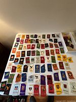 Photo showing a variety of colorful tobacco silk patches laid out on a white surface. The patches display country names and various designs including coats of arms and symbols.