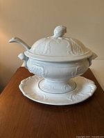 Front view of covered tureen on underplate with ladle resting in rim notch
