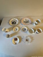 Overview of all the commemorative items on table, showing two large plates, several small dishes, tea cups, and a small creamer pot.