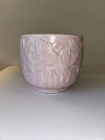 Side view of the pink planter showing embossed floral leaf design and round shape.