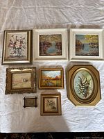 All eight vintage framed paintings laid out on white cloth, showing variety in scenes and frames.