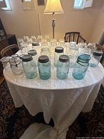 Overview of all mason jars on a round table showing both blue and clear jars of various sizes and shapes, some with lids.