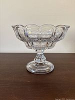 Front and side view of the large clear glass pedestal dish showing scalloped edges and rectangular pressed patterns in glass.