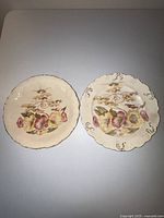 Pair of two vintage S F & Co ceramic plates showing floral designs and scalloped rims with gold accents on a white tabletop.
