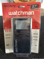 Front view of Sony Watchman FD-230 portable black and white TV in original sealed packaging, showing brand, model, and key features.