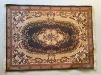 Full view of the miniature carpet showing classic Aubusson floral and ornate pattern bordered with fringe edges.