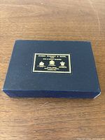 Black textured presentation box with gold and black James Purdey & Sons label on lid featuring store location.