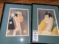 Two framed Asian art prints side by side on floor, showing portraits of men in traditional attire, framed with black frame, light blue matt border