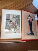 Image of two framed Asian artworks side by side on wooden floor, showing the first artwork depicting a traditional scene and the second with two women in traditional clothing.