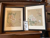 Two framed Asian silk artworks with flower designs placed side by side in a box.