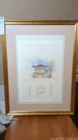 Full view of the framed Asian wall art print showing the gold frame, white matting, and detailed architectural drawing of a Japanese building.