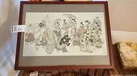 Framed Asian wall art print on display showing parade scene with multiple figures and lion dance