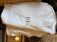 Folded white matelassé cotton bedspread with circular and diamond motifs on surface