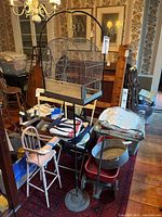 Full view of the metal bird cage hanging on the tall metal stand in a room with various furniture and items around.