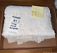 Folded crochet bedspreads in a box with labeling showing 'Vintage Crochet Bedspreads'.