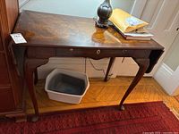 Front view showing burl veneer surface, single drawer with keyhole, cabriole legs, and contents on table.