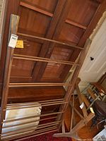 Photo showing the full vertical view of the vintage wooden clothes drying rack leaning against furniture, highlighting the multiple horizontal slats and A-frame support structure.