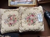 Pair of embroidered floral pillows with pink, peach, white flowers and beige ornate borders, shown stacked