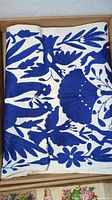 Folded view of the embroidered table runner showing bold blue floral and animal leaf patterns on white fabric.