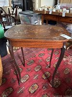 Front view of the vintage wooden end table showing the curved legs and inlaid design on top surface with signs of wear and damage.