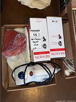 Photo of all items in the lot in a box showing two Revlon retail boxes, one fabric steamer and a red hot water bottle