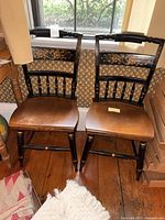 Pair of Hitchcock chairs front view showing wooden seats, black painted finish, and floral design on top backrest