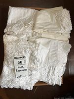 Pile of white and cream pillowcases with various lace edges and embroidery detailing packed in a box