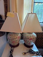 Two matching ceramic floral table lamps with beige fabric shades on a white table.