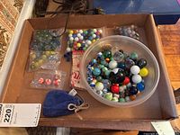Lot contents showing assorted glass marbles of varying sizes and colors with plastic bags and a blue pouch inside a cardboard box
