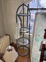 Full view of the metal display stand showing all five round glass shelves and the arched metal frame.