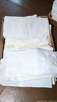 Photo showing a box of folded white pillowcases with lace and embroidery details