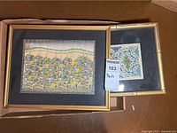 Two framed prints laid on the floor, one showing a procession scene with elephants and the other a decorative patterned design with a bamboo style frame.